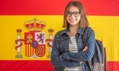 teenage-girl-glasses-wears-backpack-stands-smiling-front-flag-spain_341862-673